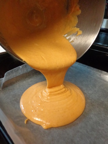pumpkin roll batter being poured into jelly roll pan