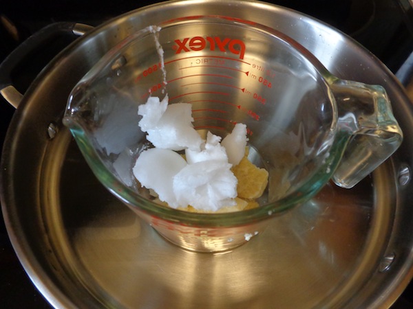 skillet filled with water with a large glass measuring cup with chapstick supplies