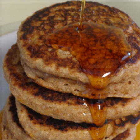 stack of cinnamon applesauce pancakes being drizzled with maple syrup