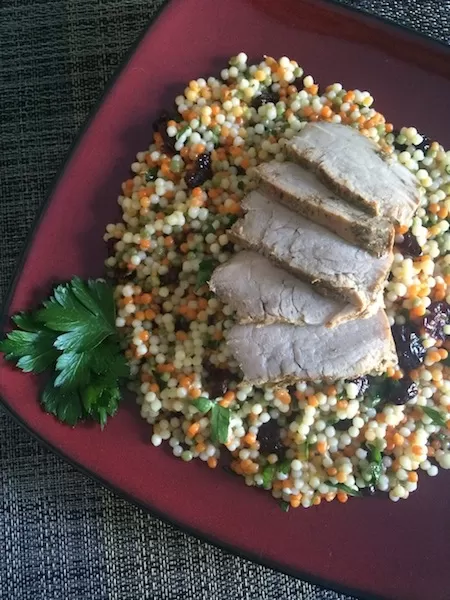 slices of pork tenderloin on a bed of multi-color cranberry lemon couscous