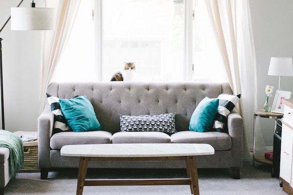 room with a large window filled with gray furniture with turquoise accents - simple tips to eliminate the stress of hosting as an introvert