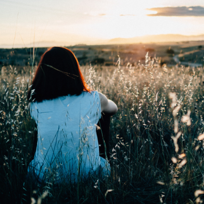 woman sitting in grassy hill watching sunset