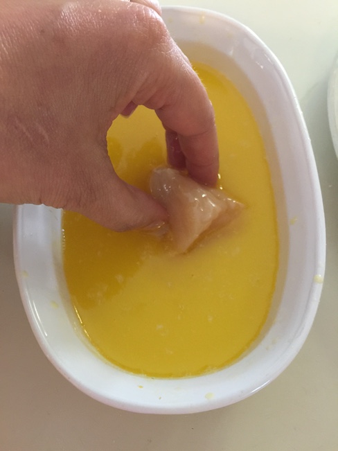 hand dipping chicken nugget into butter