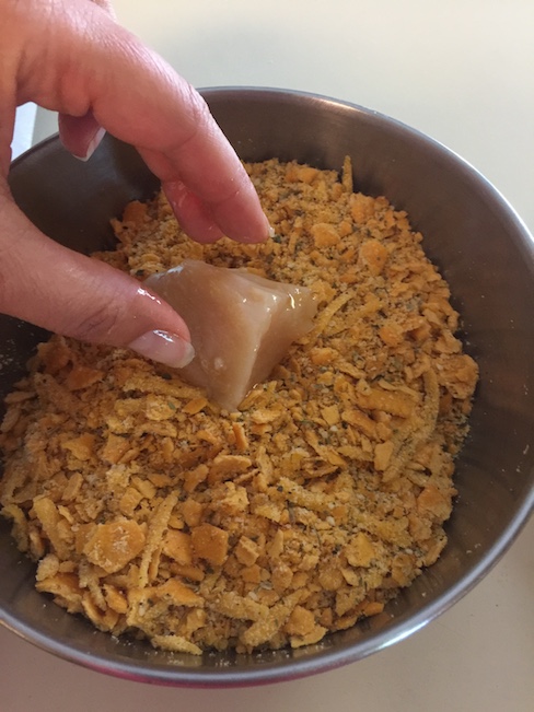 hand dipping chicken nugget into breading