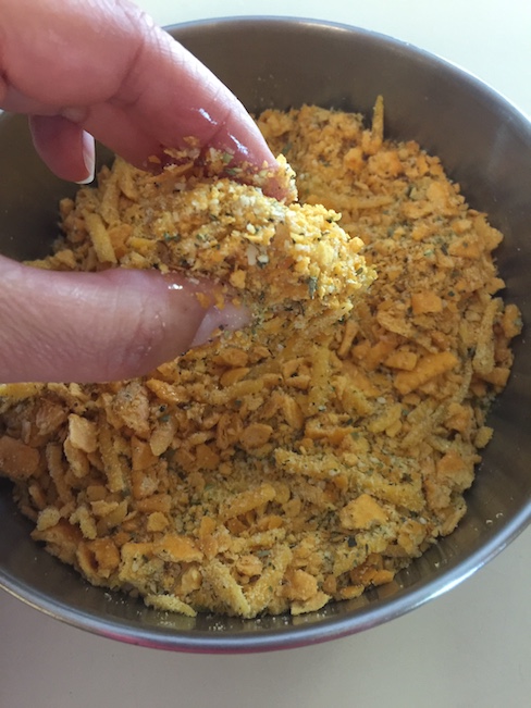 hand dipping chicken nugget into breading