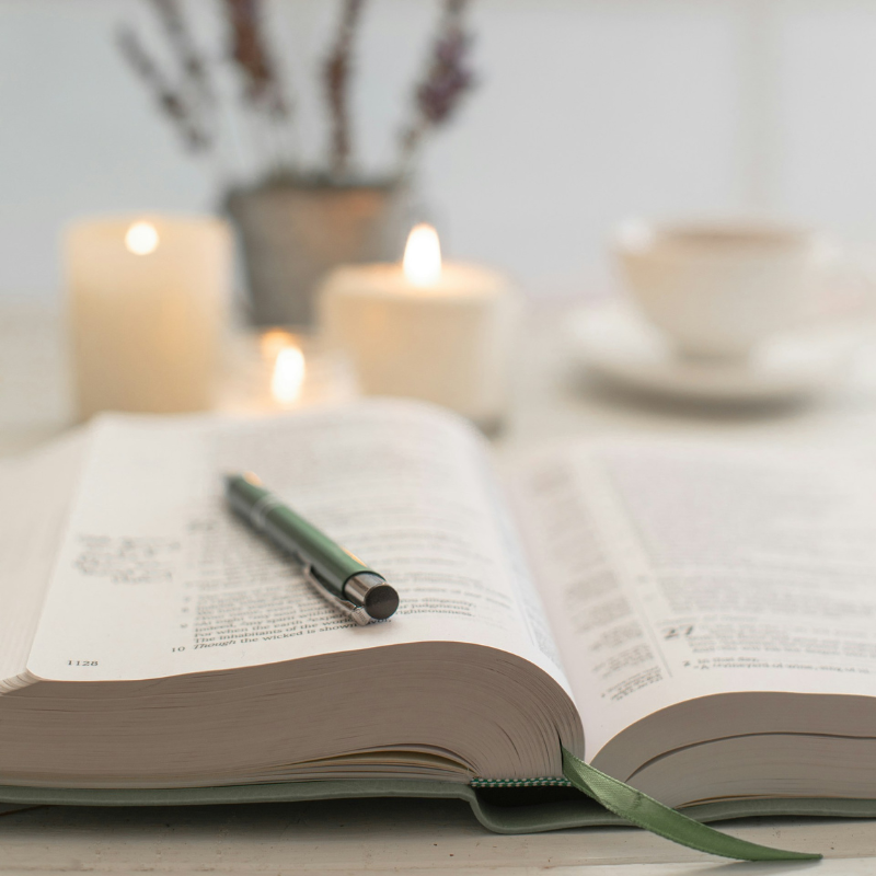 open bible sitting beside candles and cup of tea
