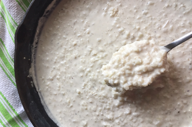 spoon full of riced cauliflower risotto over top of cast iron skillet