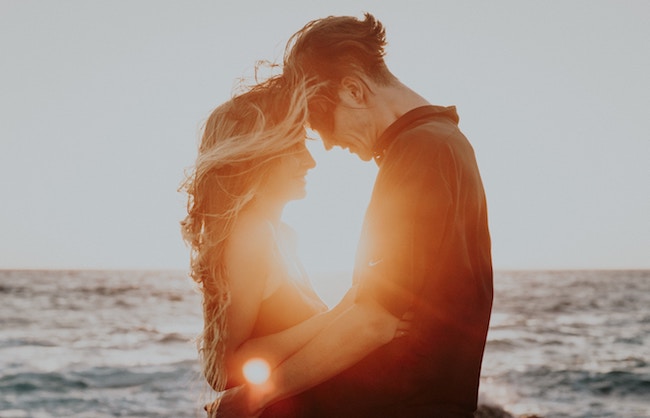 man and woman standing by ocean during golden hour