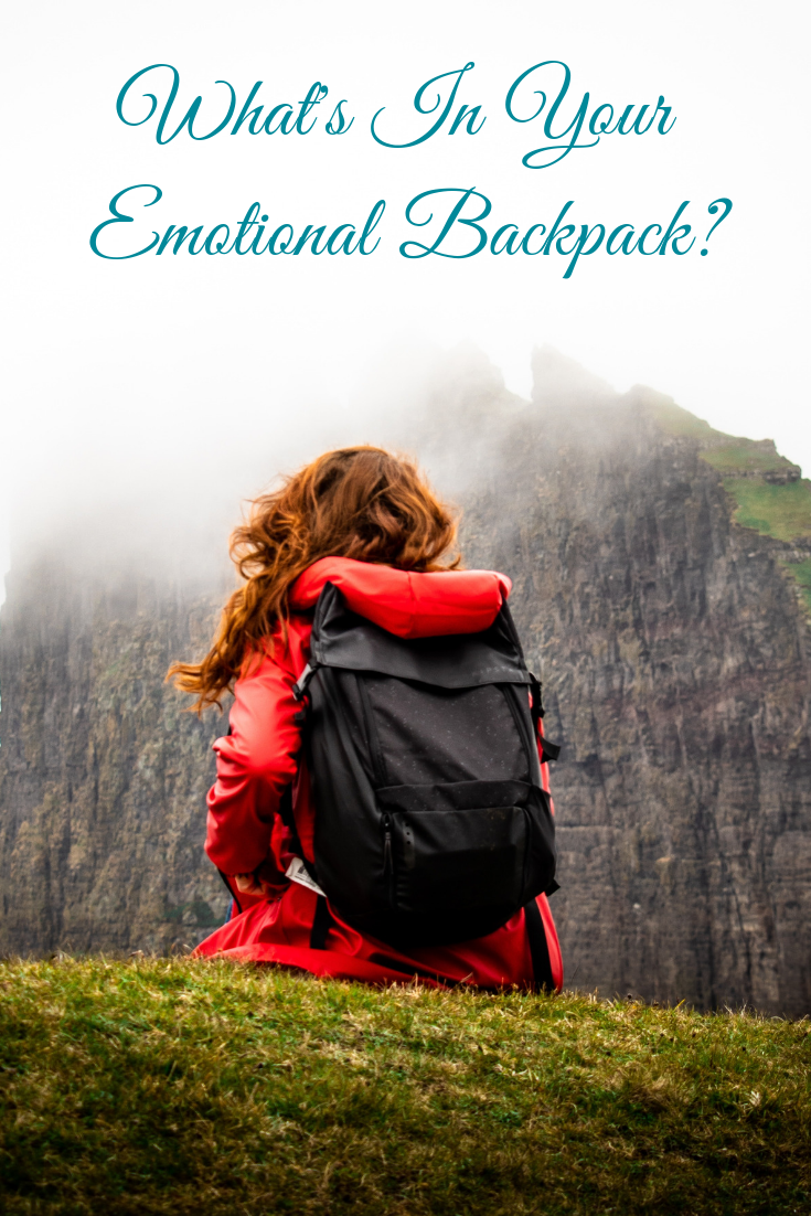 woman in a red coat with black backpack looking at a mountain