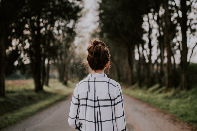 woman walking down a road with trees on the both sides