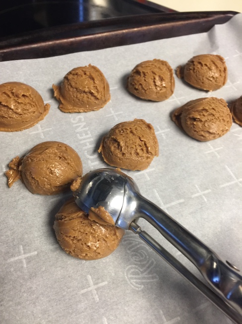 peanut butter balls being scooped onto a baking sheet