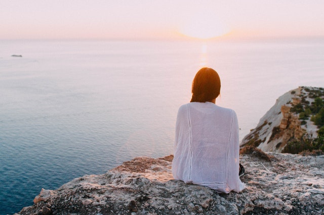 back view of woman sitting on a rock overlooking beach