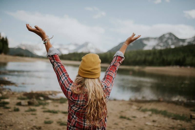 blonde headed woman wearing a beanie and flannel with outstretched arms