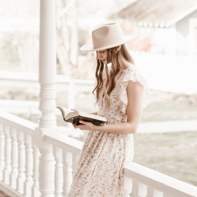 woman leaning on porch railing reading her bible