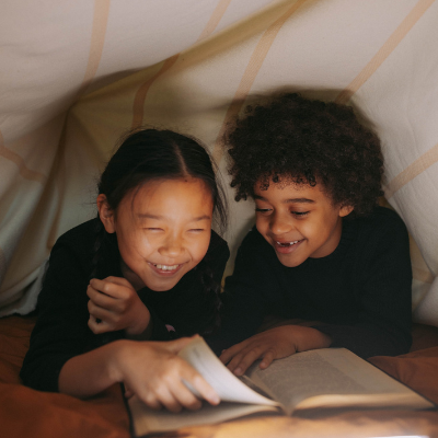 two kids reading a book under a sheet fort
