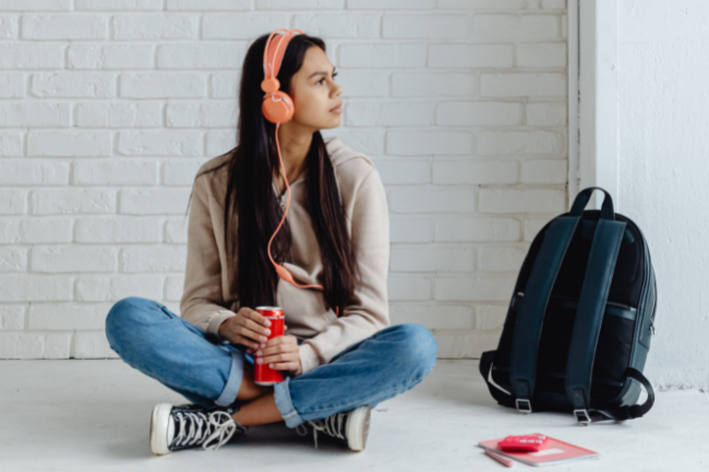 young woman with headphones sitting cross legged in front of white brick wall