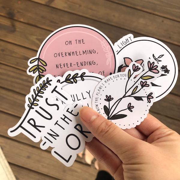hand holding white and pink stickers with flowers and bible verses 