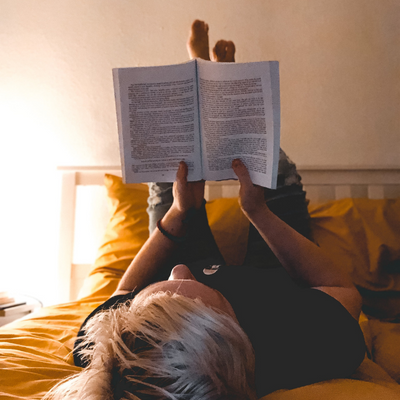 person lying in bed with feet in the air reading a book