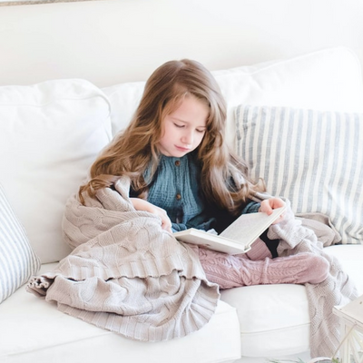 little girl sitting on a couch reading a book