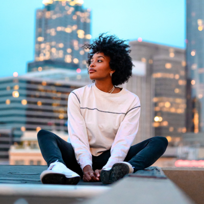 black woman sitting on top of a building in front of skyscraper