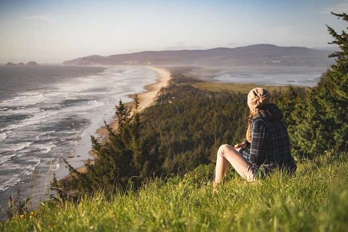 woman sitting on a grassy hill looking at the ocean