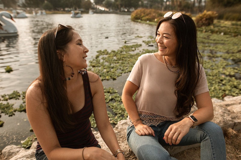 two women sitting on the edge of a pond talking