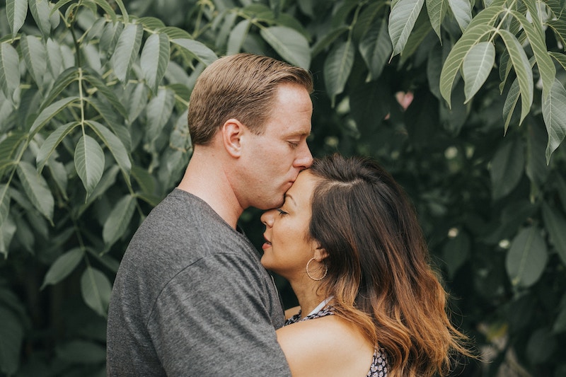 couple hugging while standing in front of green leaves