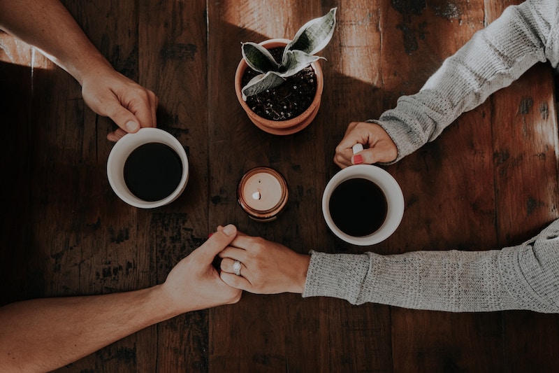 overhead view of couple holding hands while drinking coffee