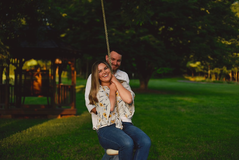 man standing behind smiling woman on a tree swing