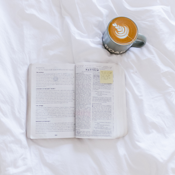 open bible and cup of coffee on top of a white comforter