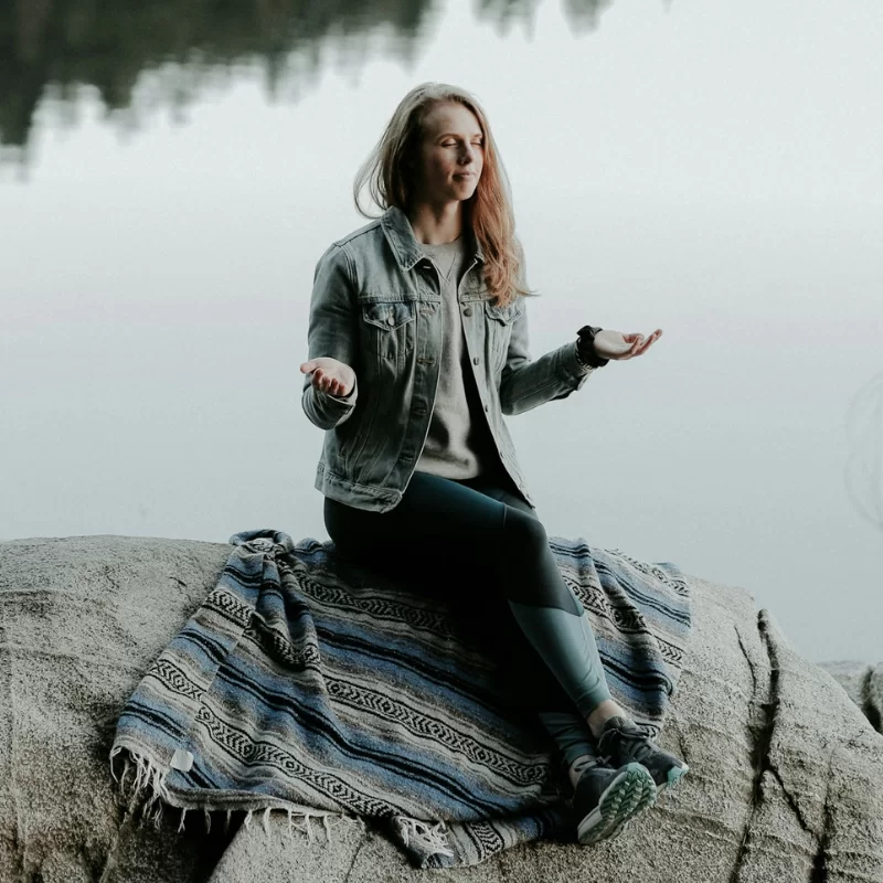 woman with opened hands praying on rock at the lake