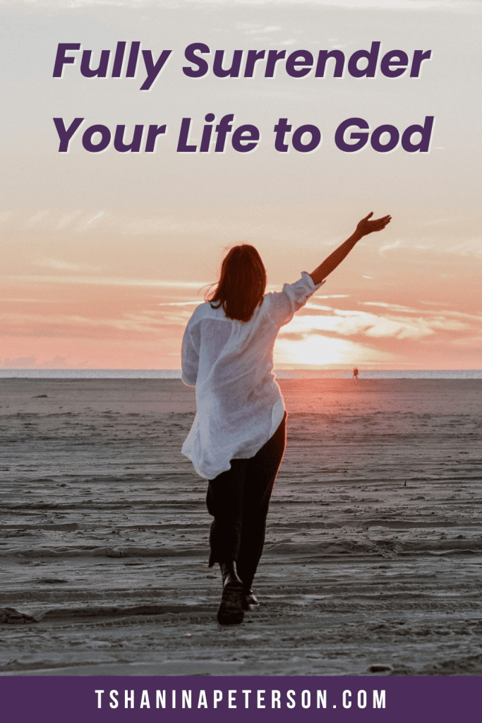 woman standing on a sandy beach at sunset with her arm outstretched 