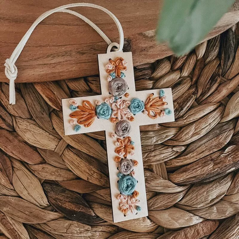 small cross with pink, blue and gold flowers embroidered on it