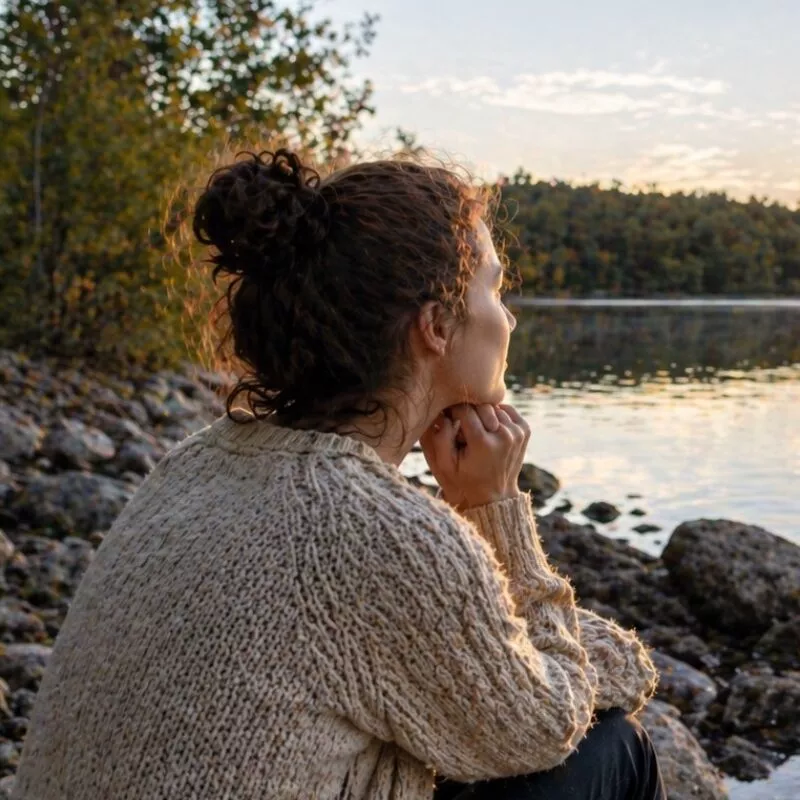Woman sitting by a peaceful lake at sunset reflecting during a difficult season