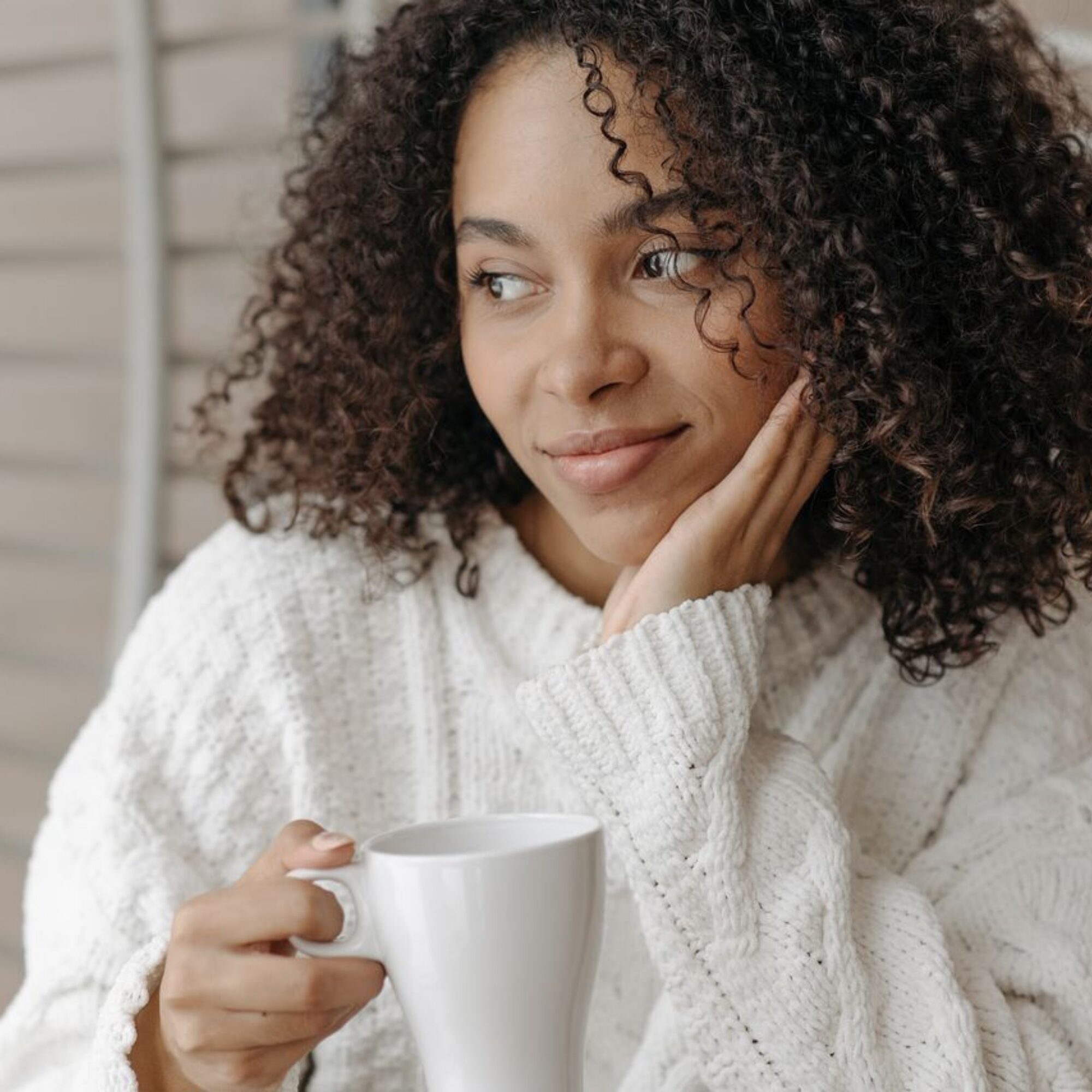 Woman holding a coffee mug and looking thoughtfully out a window